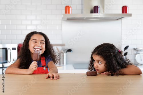 Little girls at kitchen counter eating ice cream bars