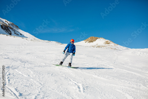 Image of sports man wearing blue jacket, helmet with snowboard riding on snowy slope