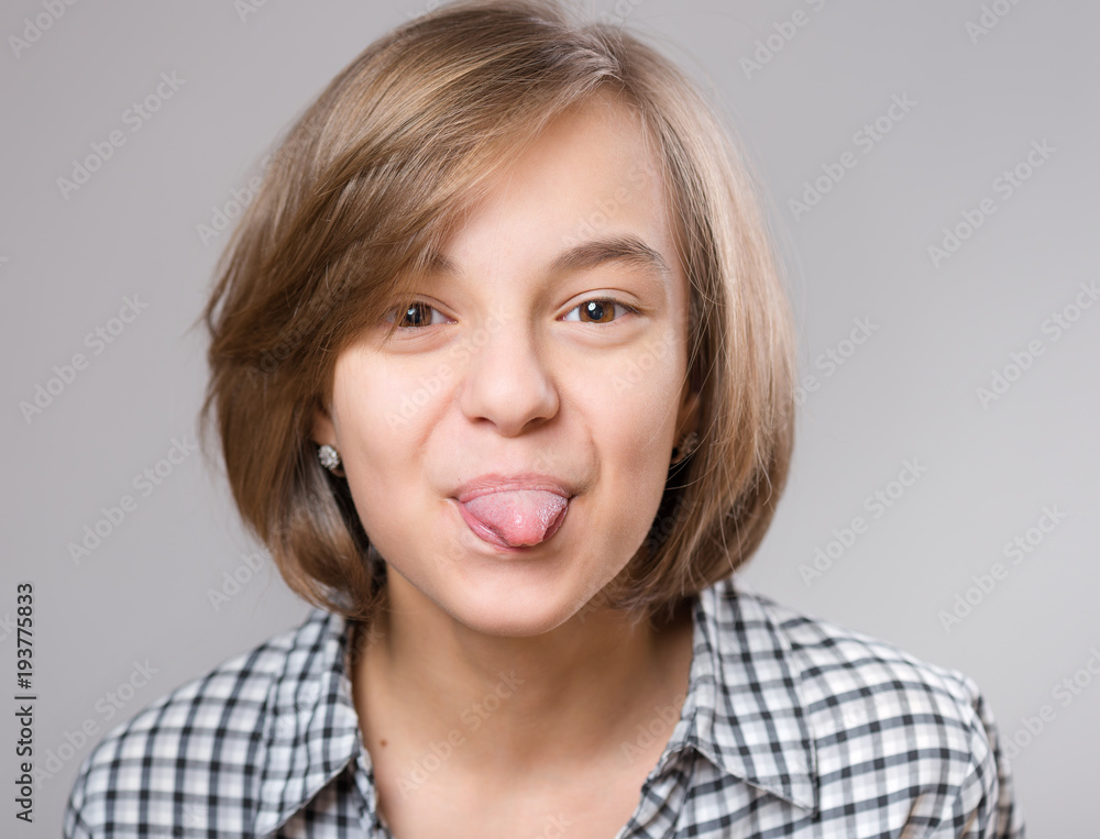 Emotional portrait of nice little girl showing her tongue. Funny teenager puts out tongue, on gray background. Emotional portrait of nice little girl showing her tongue. Funny teenager puts out tongue, on gray background.