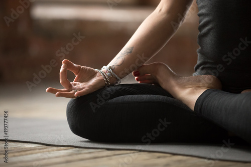 Fototapeta Naklejka Na Ścianę i Meble -  Young sporty woman practicing yoga, doing Padmasana exercise, Lotus pose, with mudra gesture, working out, wearing sportswear, black pants and top, indoor close up, yoga studio