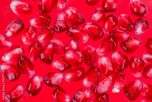 Ripe pomegranate seeds on the red background.