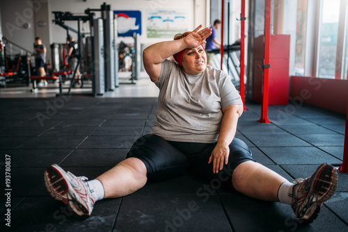 Tired overweight woman sits on the floor in gym