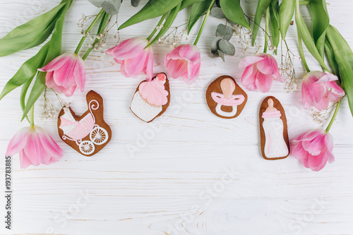 A composition for newborns on a wooden white background with pink tulips, hearts and a cookies. It's a girl.
