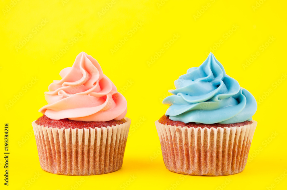 Cupcake red velvet with blue and pink whipped cream on yellow background. Picture for a menu or a confectionery catalog. Top view.