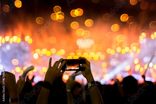 Crowd holding smartphone at concert stage lights and people fan audience silhouette raising hands in the music festival rear view with spotlight glowing effect bokeh