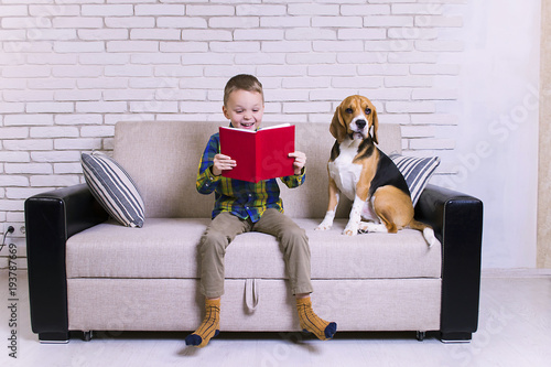 funny boy reading a book with a dog on the couch