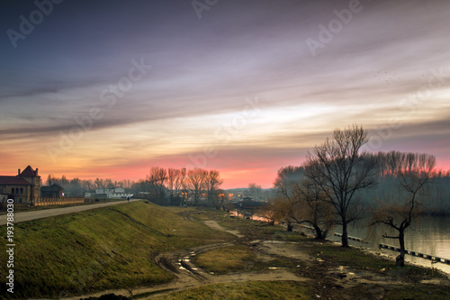 Silhouette of a lonely man in distance in sunset at the river bank