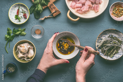 Female hands making marinate for chicken meat meal on kitchen table background with ingredients in bowls , top view. Dieting cooking eating and healthy food concept photo