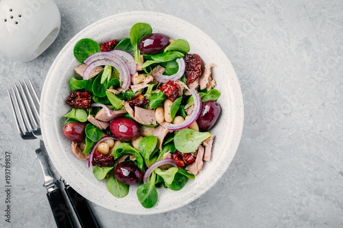 salad with white beans, tuna, olives, red onions and dried tomatoes with green lettuce leaves
