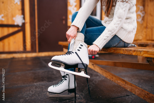 Female person sitting on bench and wears skates