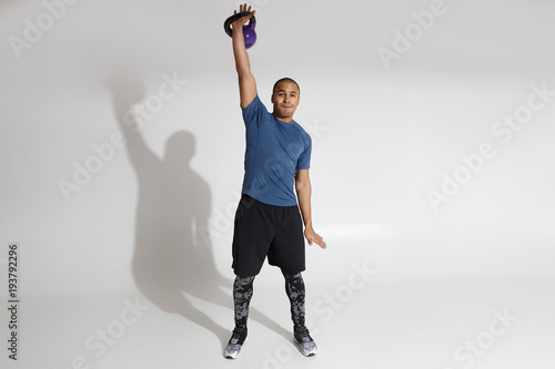 Full lenght portrait of fit young African American man exercising with dumbbells in studio. Muscular black male model lifting heavy dumbbell, building up muscles. Sports, fitness and healthy lifestyle