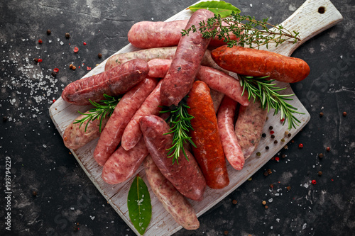 Foto Freshly made raw breed butchers sausages mix in skins with herbs on white cutting board