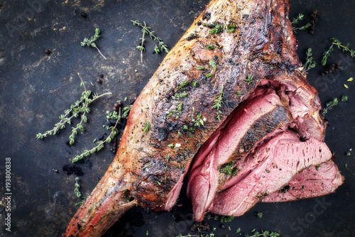Marinated barbecue aged leg of venison sliced with herbs as top view on a rustic board