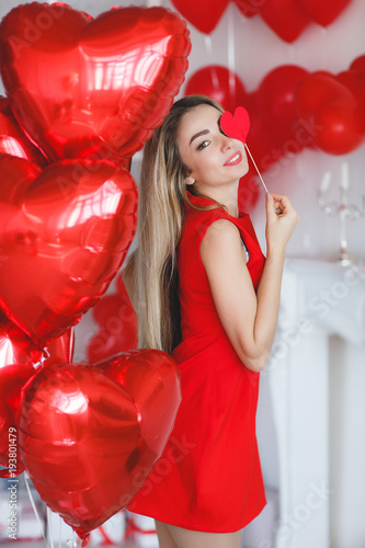Beauty Valentine's Day Woman with red balloons. Fashion Model Girl face profile Portrait with red balloons in the shape of heart in her hand. Red Lips and Nails. Pink blurred background. 