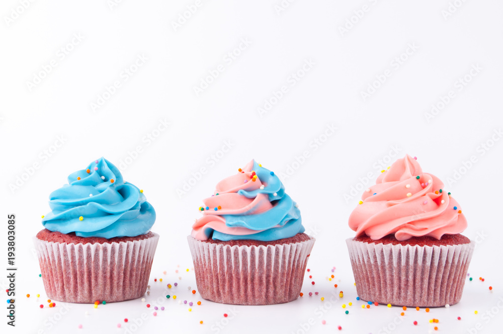 Cupcake red velvet with blue and pink whipped cream decorated with colorful sprinkles on white background.