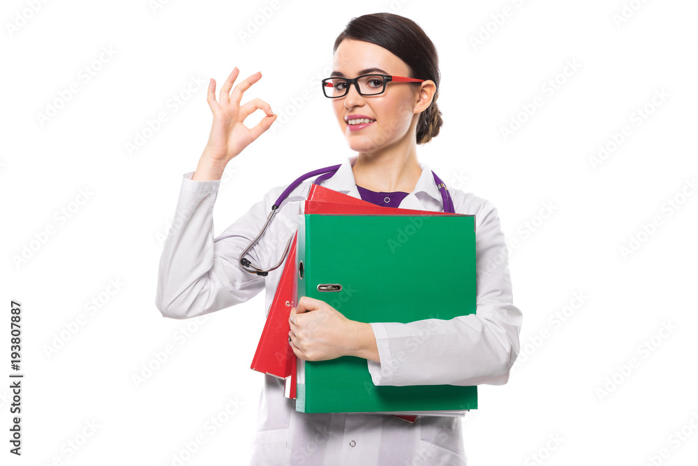 Successful young woman doctor with stethoscope holding binders in her hands showing ok in white uniform on white background Successful young woman doctor with stethoscope holding binders in her hands showing ok in white uniform on white background