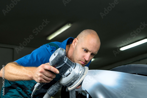 Grinder in the hands of a man who sharpen a car varnish in the car shop.