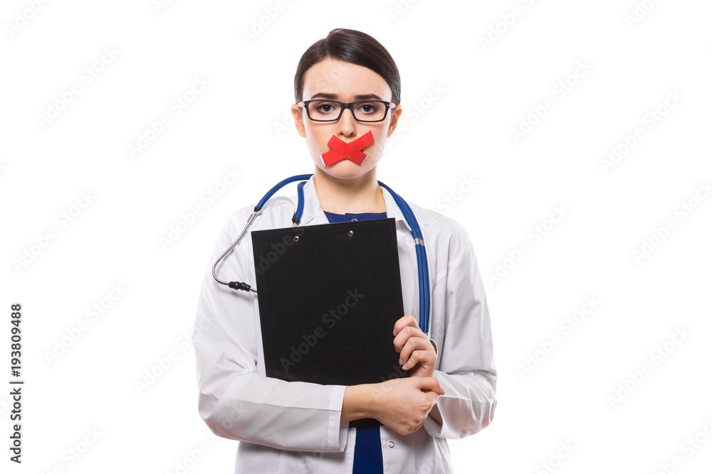 Young woman doctor with stethoscope holding clipboard in her hands with taped lips in white uniform on white background Young woman doctor with stethoscope holding clipboard in her hands with taped lips in white uniform on white background