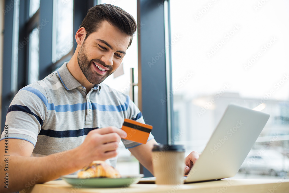 Happy cheerful man looking at his credit card Happy cheerful man looking at his credit card