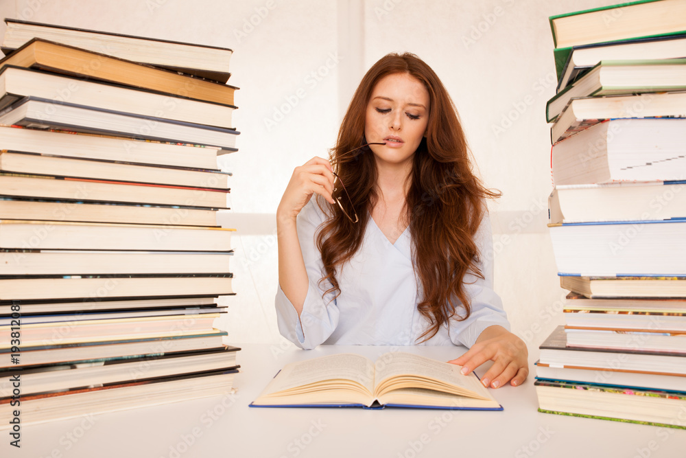 attractive young woman studies wtih hugr book piles on her desk attractive young woman studies wtih hugr book piles on her desk
