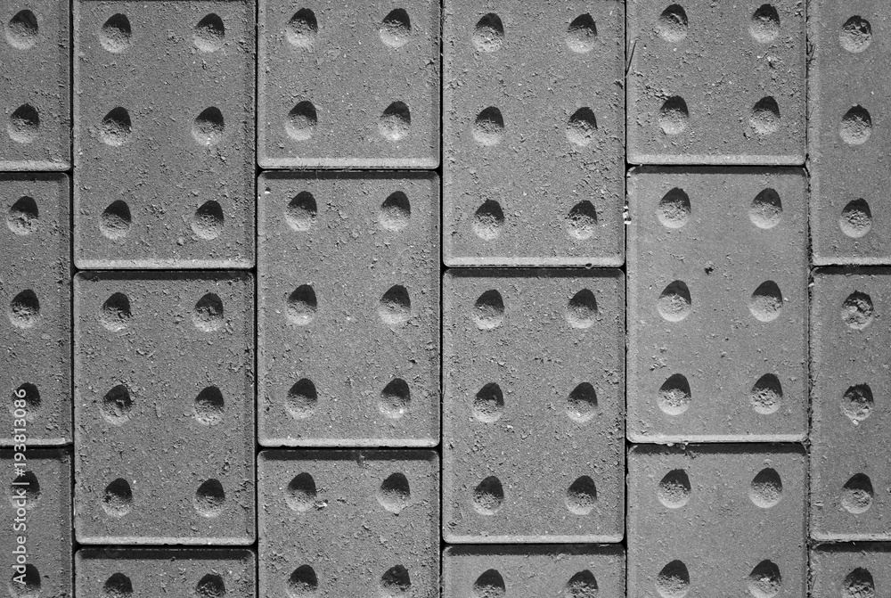 Tactile paving bricks with shadow detail photographed and processed in black and white to provide an abstract background