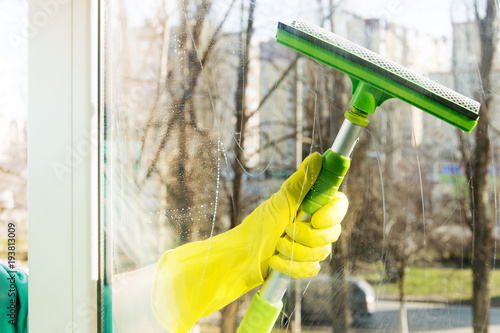 Hand in a yellow glove clears the window with a green scraper