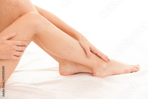 Long and slim woman legs on white sheets in bed isolated over white background