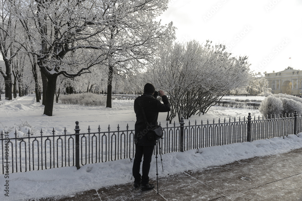 Photographer on snow-covered streets at sunny day, frosted trees and accidental people.