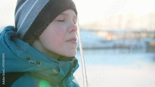 A boy licking an icicle. Snowy frosty Sunny day. Fun and games in the fresh air.