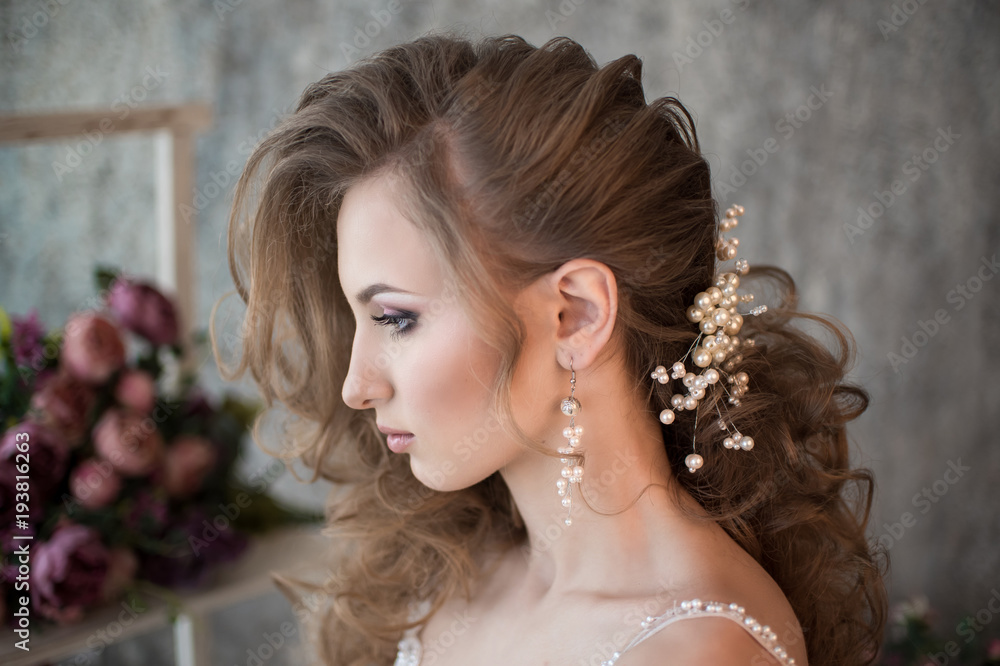 Portrait of a beautiful bride in a profile. Wedding hairstyle. Curls. Decoration from pearls. Flowers. Gray background.