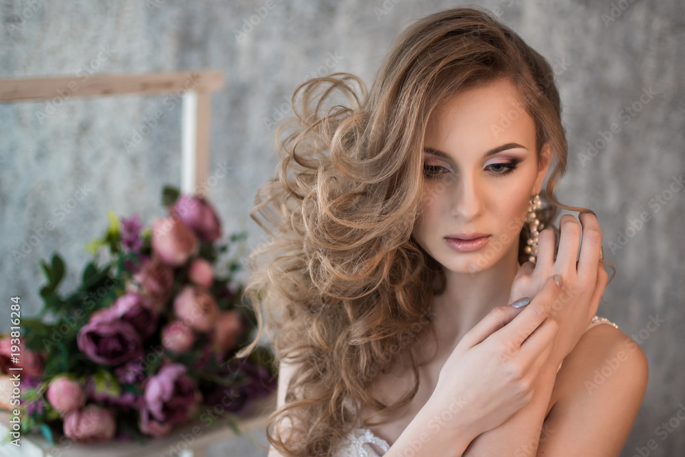 Fototapeta premium Portrait of a beautiful bride. Hands at the face. Wedding make-up. Volume hairstyle. The curls. Bouquet of flowers.