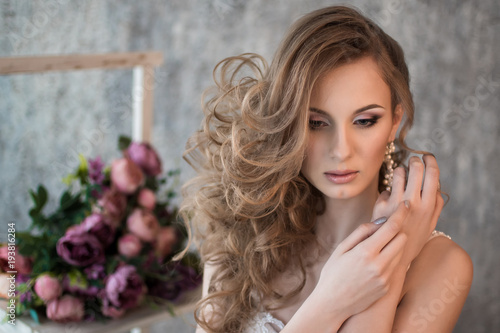 Portrait of a beautiful bride. Hands at the face. Wedding make-up. Volume hairstyle. The curls. Bouquet of flowers.