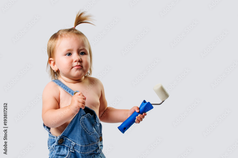 Little, cute baby girl dressed in denim overalls playing with paint roller Little, cute baby girl dressed in denim overalls playing with paint roller