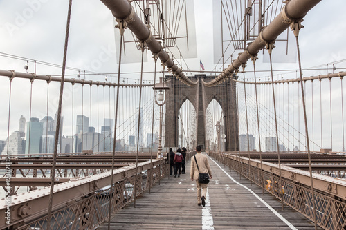 Man walking on pedestrian path across Brooklyn bridge. New York City Manhattan downtown with skyscrapers over East River panorama as seen from Brooklyn bridge.