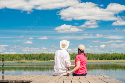 young couple with a fishing rod sitting on a wooden pier near the lake, rear view