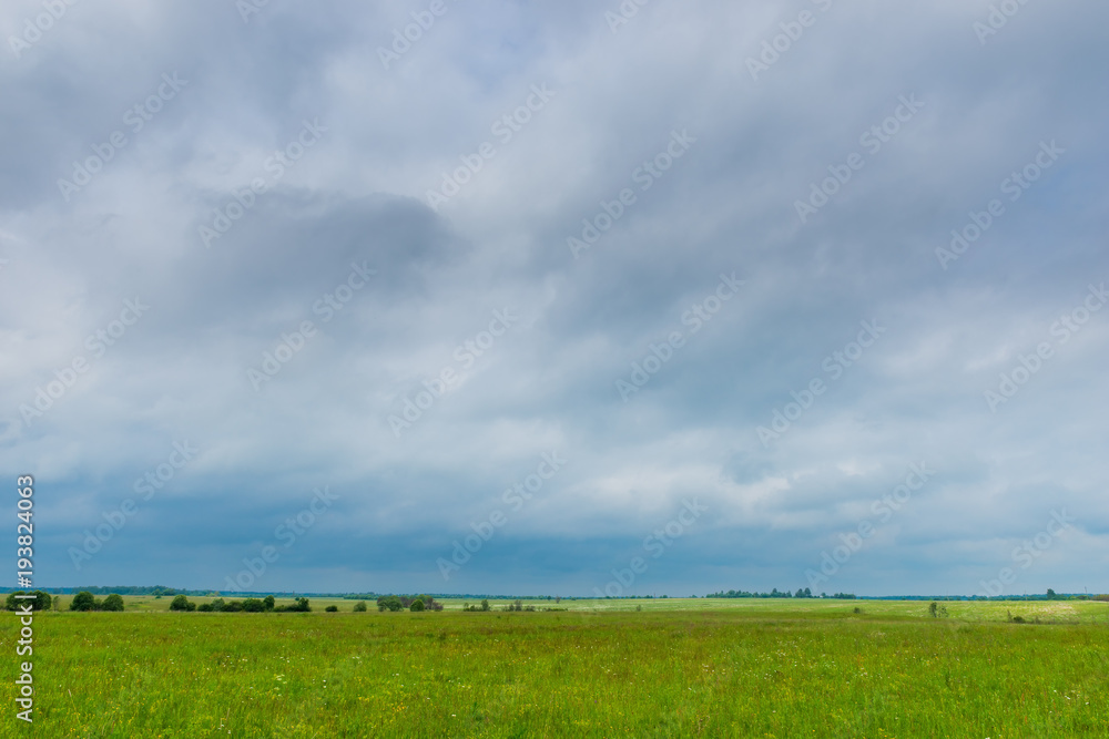 Fototapeta premium Dark rainy clouds hang on a green spring field in the countryside