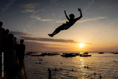 People jumping on water in Stone Town with beautiful landscape sunset in background. Zanzibar, Tanzania - Africa.