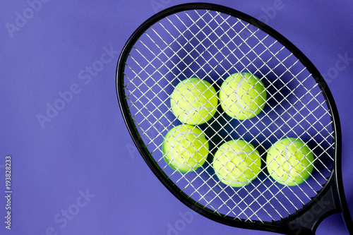 Tennis balls under black racquet. Violet background. Concept sport. © Olha Kozachenko