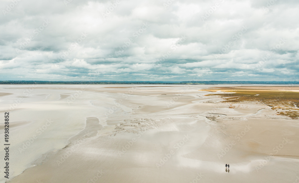 Unidentified people walking on sands during low tide outside Le Mont Saint-Michel tidal island in Normandy, France