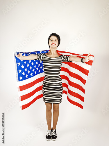 Portrait of a happy young brunette woman in black and white dress against the background of the American flag