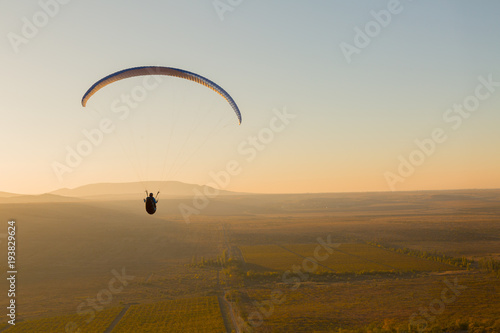 Paraplan flying over a field at sunset