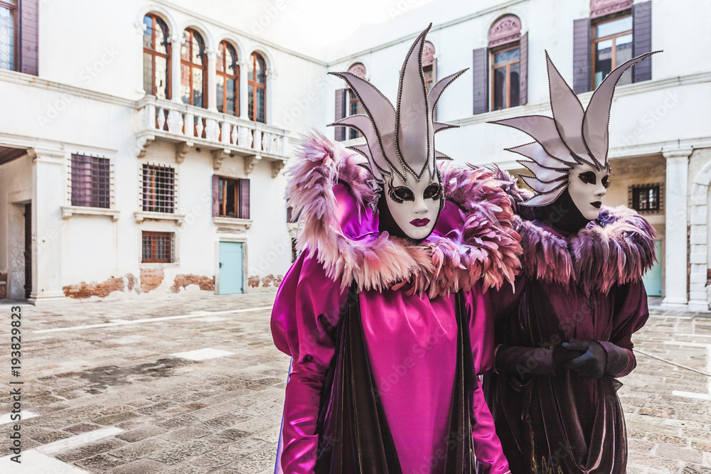 VENICE, ITALY - FEBRUARY 10 2018: Pair of white and purple colored carnival masks inside a small courtyard VENICE, ITALY - FEBRUARY 10 2018: Pair of white and purple colored carnival masks inside a small courtyard