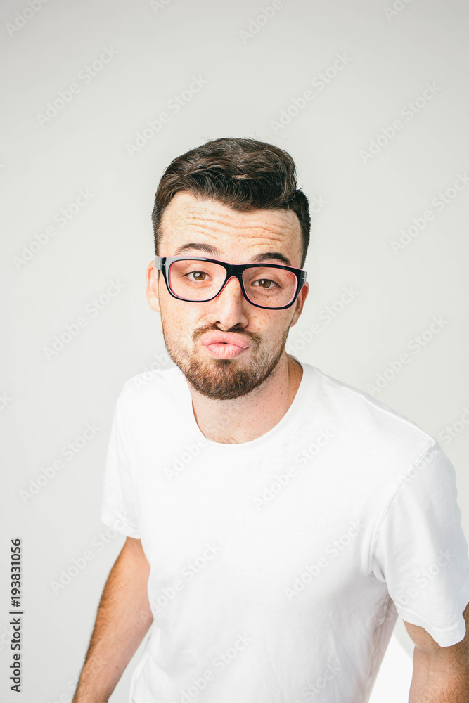 A vertical portrait of a dark-haired and bearded man standing at white wall wears glasses and looking straight to the camera. He has very strange and arrogant sight. Close up. Cut view A vertical portrait of a dark-haired and bearded man standing at white wall wears glasses and looking straight to the camera. He has very strange and arrogant sight. Close up. Cut view
