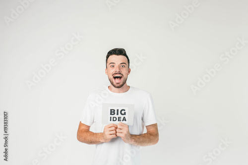 Such a beautiful photo of a young man standing in white room in white t-shirt and showing an inscription of Big Idea and he really has it, it has just come to his mind.