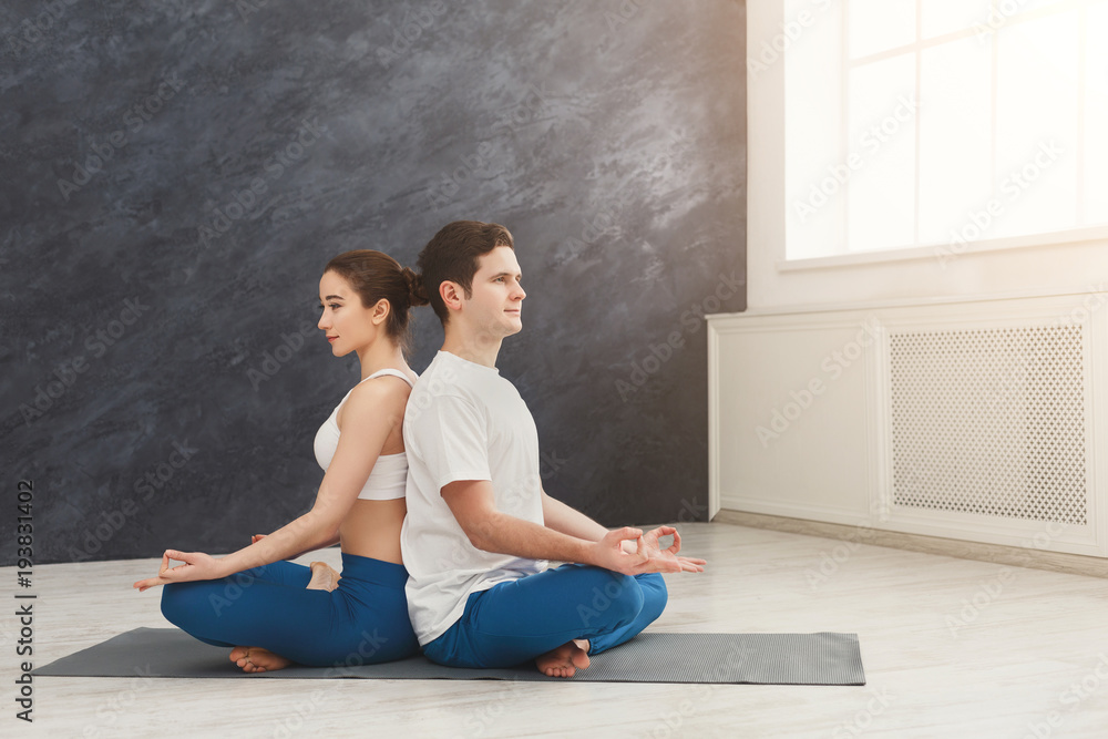 Young couple meditating together, back to back Young couple meditating together, back to back