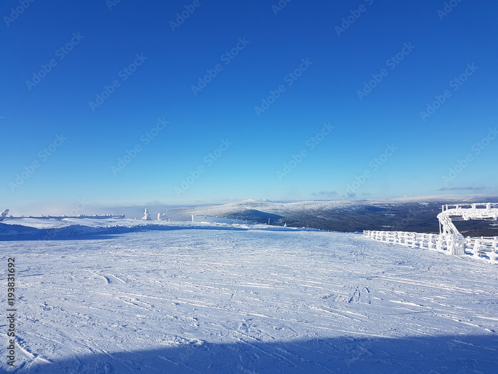 Top of a snowy mountain used as skiing resort, with blue sky and tracks from the skiers