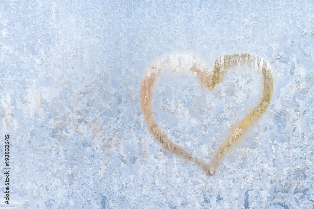 Heart on a frosty winter in the frozen patterns of ice window