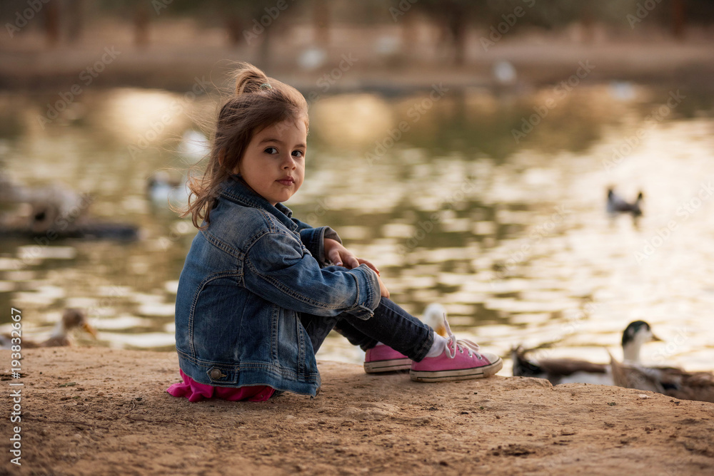 Cute little girl seating near lake witn ducks Cute little girl seating near lake witn ducks