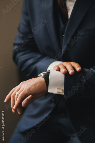 A man in a blue stylish suit looks at his watch. Hands close-up with manteds and gold cufflinks