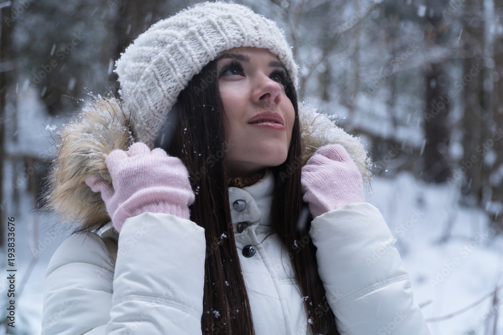 Beautiful girl with long dark hair in a white jacket walking in a winter forest during a snowfall Beautiful girl with long dark hair in a white jacket walking in a winter forest during a snowfall